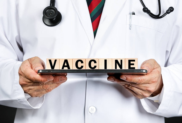 A doctor in white coat holding wooden blocks spelling vaccine. Covid-19 prevention concept. - Photo, Image
