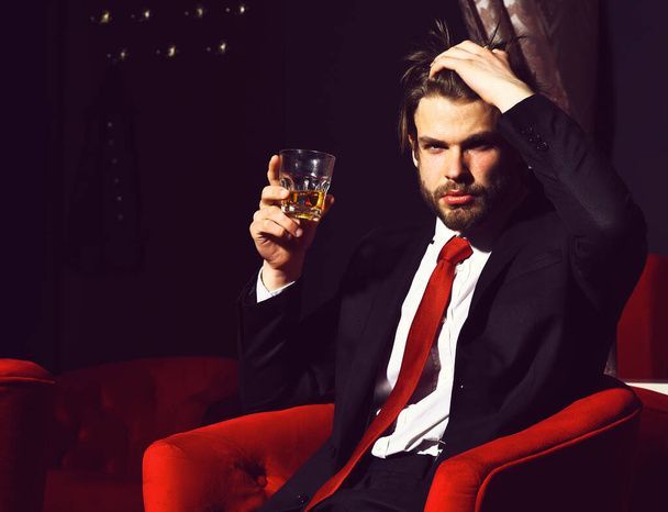 bearded man, businessman holding glass of whiskey in red chair - Foto, afbeelding