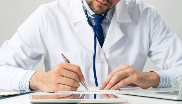 Successful therapist something writing at notepad. Physician in medical uniform with stethoscope working in office. Professional examination and diagnosis in modern clinic. Health care and treatment - Foto, Imagen