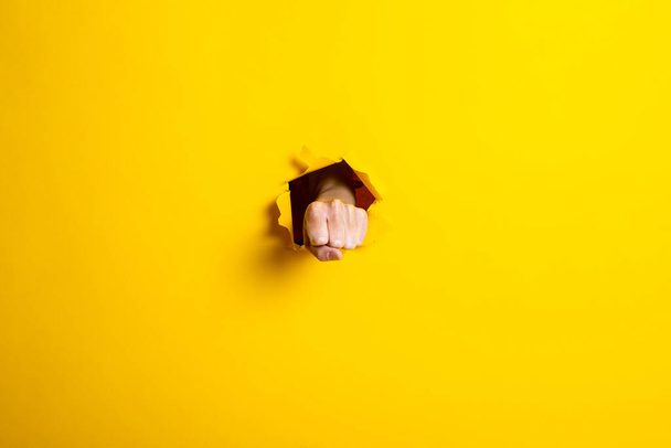 Male fist punched a hole in a yellow background. Blow, strength, masculine strength - Photo, Image