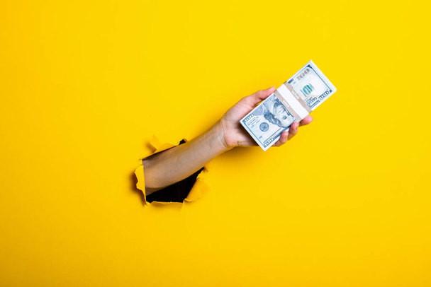 Woman's hand holds a bundle of one hundred dollar bills on a yellow background. - Photo, Image