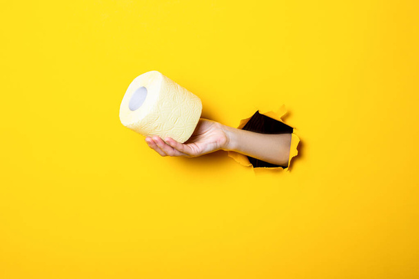 La mano de la mujer sostiene papel higiénico amarillo sobre fondo amarillo roto
. - Foto, Imagen