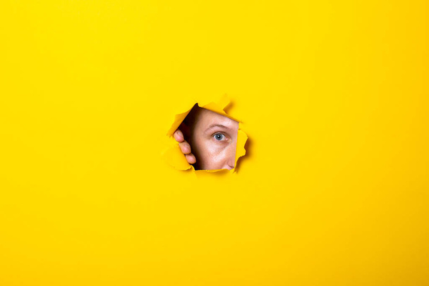 Young man peers evilly into the hole of torn yellow background - Φωτογραφία, εικόνα