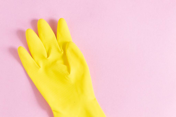 A closeup shot of a yellow plastic glove on a pink background - Foto, afbeelding