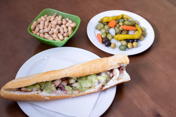 seppie con salsa mery baguette sandwich su un piatto accanto a arachidi e olive - Foto, immagini
