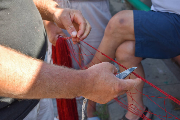 Sataman punaista kalaverkkoa leikkaava kalakauppias - Valokuva, kuva