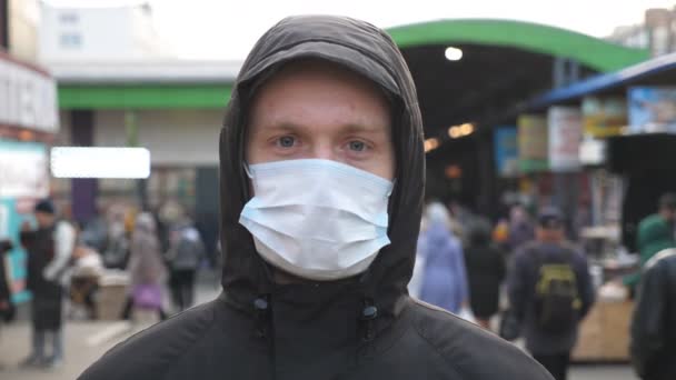 Portrait of young man with medical face mask stands at city street. Guy wearing protective mask from virus outdoor in the people crowdy. Concept of health and safety life from coronavirus pandemic - Footage, Video