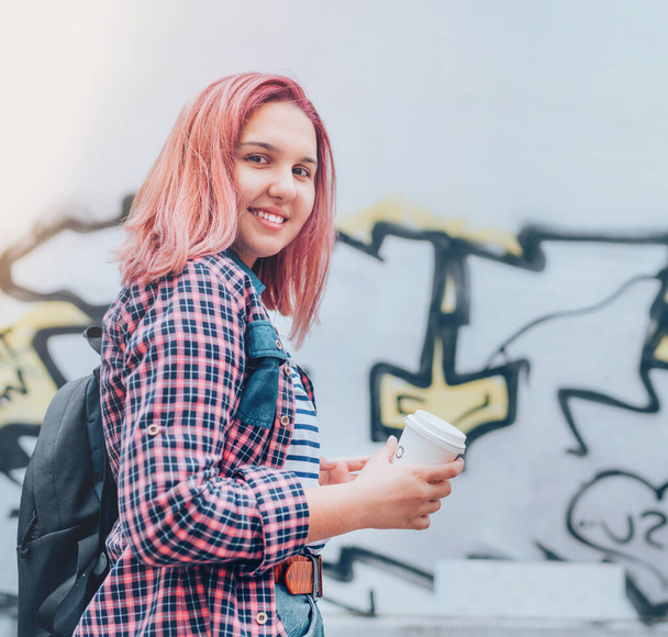 Cheerfully smiling Beautiful modern young female teenager Portrait with extraordinary hairstyle color in checkered shirt holding "coffee to go" cap.  Modern teens or cheerful students concept image - Φωτογραφία, εικόνα