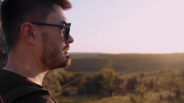 Close-up van een jonge blanke man die enthousiast naar de zonsondergang kijkt. Hij zit midden in een park in Moldavië.. - Video