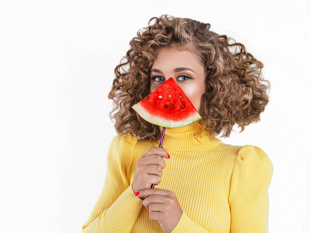Boldog fiatal lány göndör hajjal, kezében egy szelet görögdinnyével az arcán, elszigetelve a fehér háttértől. Afro lány tartja görögdinnye. - Fotó, kép