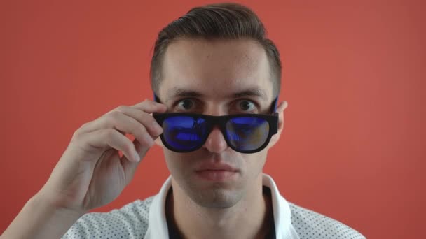 Stylish young man shocked and surprised on red color background. Man hipster in surprise shoots sunglasses and looks at the camera in surprise. - Footage, Video