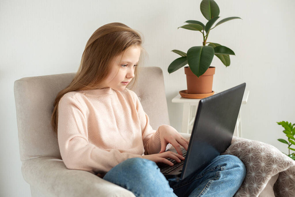 School girl sitting in armchair and using laptop at home. Education Back to school - Image - Foto, imagen