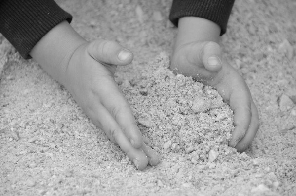 Dziecko zbiera piasek rękami - Baw się wszystkimi zmysłami i poznaj otoczenie - czarno-białe - Zdjęcie, obraz