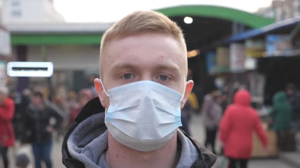 群衆の中にウイルスの屋外から保護マスクを身に着けている男。医者の顔のマスクをした若い男の肖像画が街の通りに立っている。コロナウイルスとパンデミックからの健康と安全生活の概念 - 映像、動画