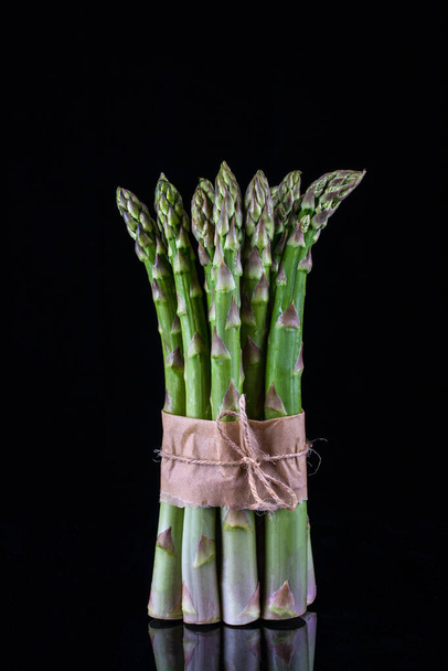 Asparagus. Bunch of fresh green asparagus tied on black background. - Foto, afbeelding