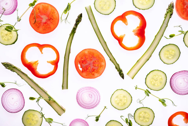 Creatief lay-out patroon gemaakt van tomatenschijfje ui komkommer asperges microgroene peper Flat lay. Voedselconcept. Groenten geïsoleerd op witte achtergrond. - Foto, afbeelding