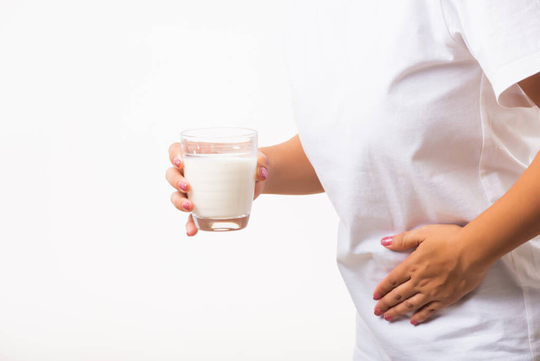 Closeup young woman intolerant use hand holding glass milk she is bad stomach ache she has bad lactose intolerance unhealthy problem with dairy food products, studio shot isolated on white background - Foto, afbeelding
