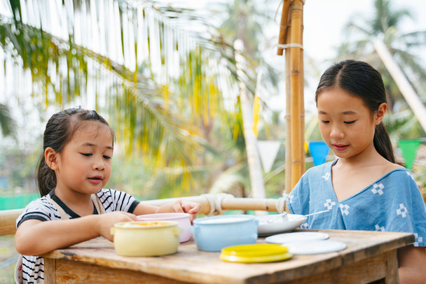 Zwei asiatische Kinder beim Mittagessen aus dem Futtermittelcontainer oder Pinto auf dem Holztisch auf dem Land. - Foto, Bild