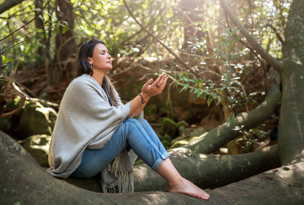Mujer meditando sola con los ojos cerrados en un bosque tranquilo con las palmas de sus manos levantadas al sol - Foto, Imagen