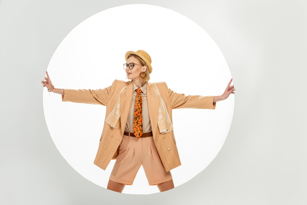 Smiling woman in beige blazer and straw hat touching round hole on white background  - Photo, Image