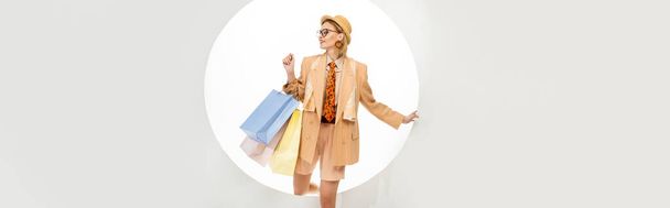 Horizontal image of smiling woman holding shopping bags near round hole on white background  - Photo, Image