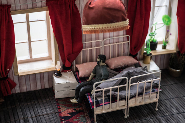 Hombre en la cama durante el día. Una casa de muñecas realista dormitorio con muebles y ventana. El virus Corona se queda en casa sea un concepto seguro. Enfoque selectivo
 - Foto, Imagen