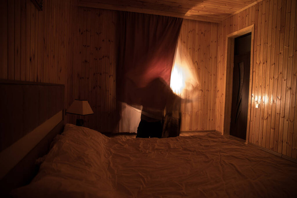 Силуэт ужаса в окне с занавеской внутри спальни ночью. Сцена ужаса. Концепция Хэллоуина. Размытый силуэт призрака - Фото, изображение
