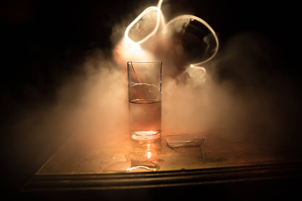 Drinken, gebroken glas concept. Gebroken bril op houten tafel bij donkere achtergrond met mist. Selectieve focus - Foto, afbeelding