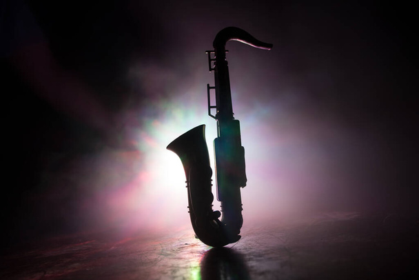 Concepto musical. Instrumento de jazz saxofónico. Alto saxo dorado miniatura con luz tonificada de colores sobre fondo nebuloso. Instrumento de música saxofónica a plena luz. Enfoque selectivo - Foto, Imagen
