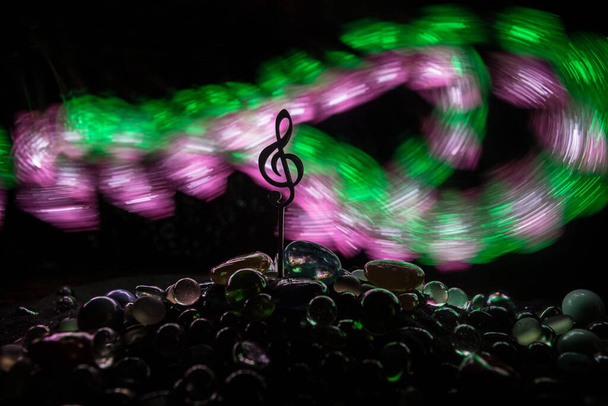 Concept musical. Symbole musical triple clef miniature en acier inoxydable avec lumière tonique colorée sur fond brumeux. Concentration sélective - Photo, image