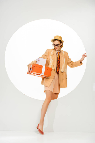 Smiling girl in straw hat and jacket holding presents near circle on white background  - Photo, Image
