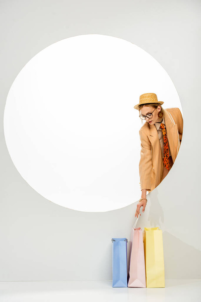 Fashionable girl holding colorful shopping bag behind circle on white background  - Foto, Imagen