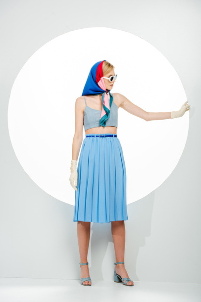 Fashionable girl in blue skirt and sunglasses touching round hole on white background  - Fotó, kép