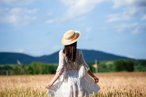 Buğday tarlasında arkadan bir kızın portresi. Buğday tarlasında beyaz elbiseli ve şapkalı güzel bir kızın portresi. Beyaz elbiseli ve şapkalı kız. Buğday tarlası. - Fotoğraf, Görsel