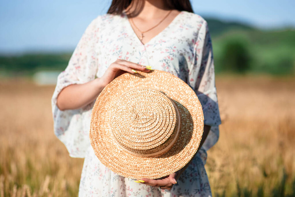 Girl holding a hat on a background of wheat field. - Photo, Image