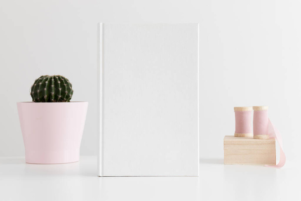 Libro blanco maqueta con cintas de seda y un cactus en una olla en la mesa blanca
. - Foto, Imagen