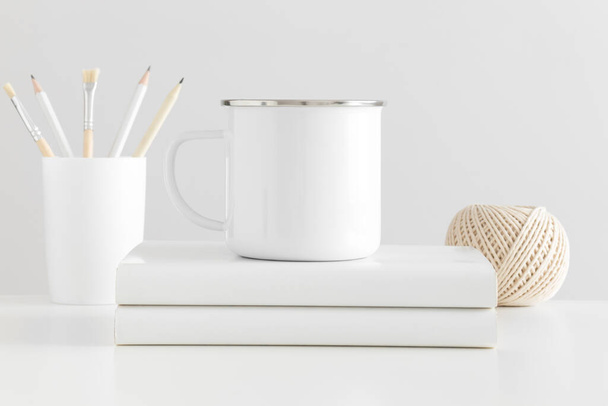 Enamel mug mockup with workspace accessories on a white table. - Photo, Image