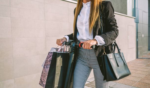 Mulher irreconhecível com sacos de compras em scooter elétrico
 - Foto, Imagem