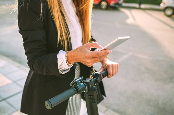 Donna d'affari irriconoscibile con e-scooter guardando il cellulare - Foto, immagini
