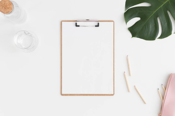 Top view of a wooden clipboard mockup with  workspace accessories and a monstera leaf on a white table. - Photo, Image
