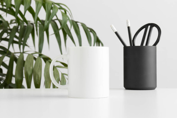 Taza de maqueta con accesorios de espacio de trabajo en una mesa blanca y una planta de palma
. - Foto, Imagen