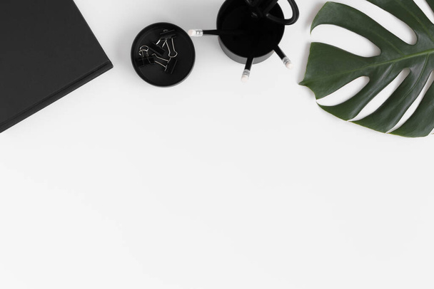 Workspace accessories and a monstera leaf on a white table.  Flat lay with blank copy space. - Фото, изображение