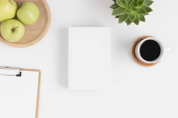 Vue de dessus d'une maquette de livre blanc avec accessoires d'espace de travail, plante succulente et pommes sur une table blanche. - Photo, image