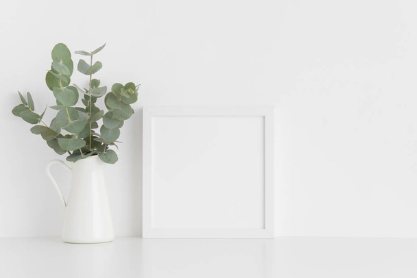 Λευκό τετράγωνο πλαίσιο μακιγιαρισμένο με μπουκέτο ευκαλύπτου σε ένα βάζο πάνω σε λευκό τραπέζι.Πορτραίτο. - Φωτογραφία, εικόνα