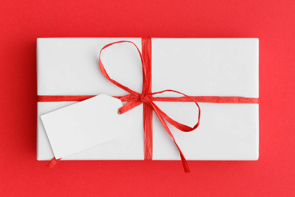 Weiße Weihnachtsgeschenk mit einem leeren Tag-Attrappe auf rotem Hintergrund. - Foto, Bild