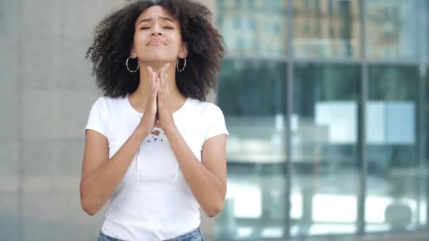 Jonge Afro-Amerikaanse vrouw maakt wens, kruist middelste en wijsvingers op handen, bidt gebalde handen in smekend gebaar. Droom is uitgekomen, meisje stuitert in extase, lacht vrolijk springend. - Video
