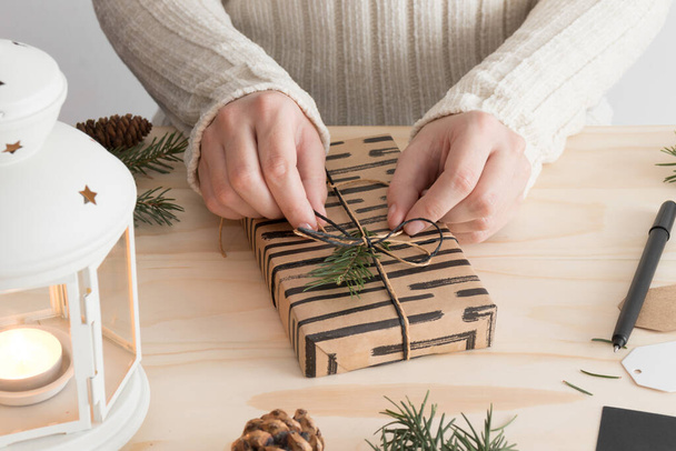 Женщина заворачивает черный рождественский подарок на деревянный стол с рождественским декором. - Фото, изображение