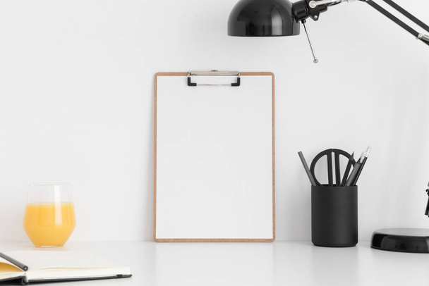 Wooden clipboard mockup wtih a notebook, lamp and workspace accessories on a white table. - Фото, зображення