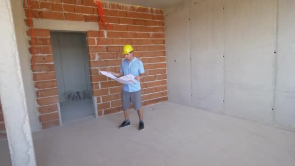 SLOW MOTION: L'uomo caucasico che indossa un cappello rigido ispeziona la casa in costruzione - Filmati, video