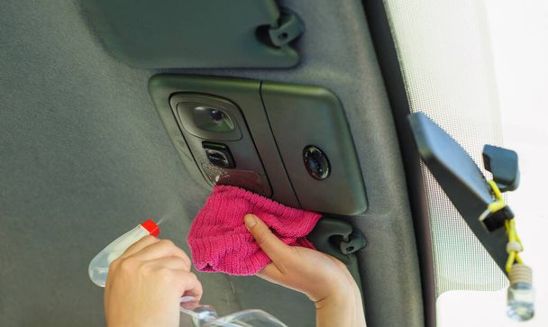 Egy nő fertőtleníti a kocsiját egy rózsaszín törlőkendővel. Megelőzni a vírust és a baktériumokat, megelőzni a kovid19-et, a koronavírust, az alkoholos fertőtlenítőt. Higiéniai koncepció otthon. - Fotó, kép